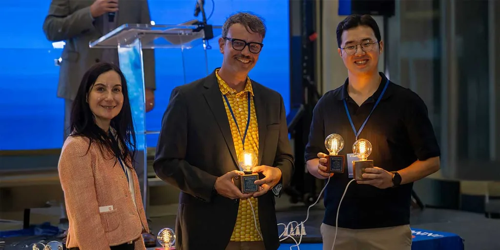 Gregory Hudalla, Ph.D., from the J. Crayton Pruitt Family Department of Biomedical Engineering and Junha Park receive their award for their ELISA test speeds project from Melissa Kuchma from UF Innovate.